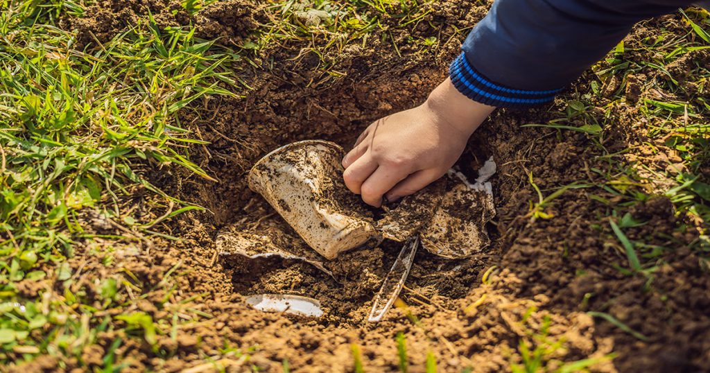 Trash in a patch of dirt and grass, showing the negative environmental impact of our waste on the environment.