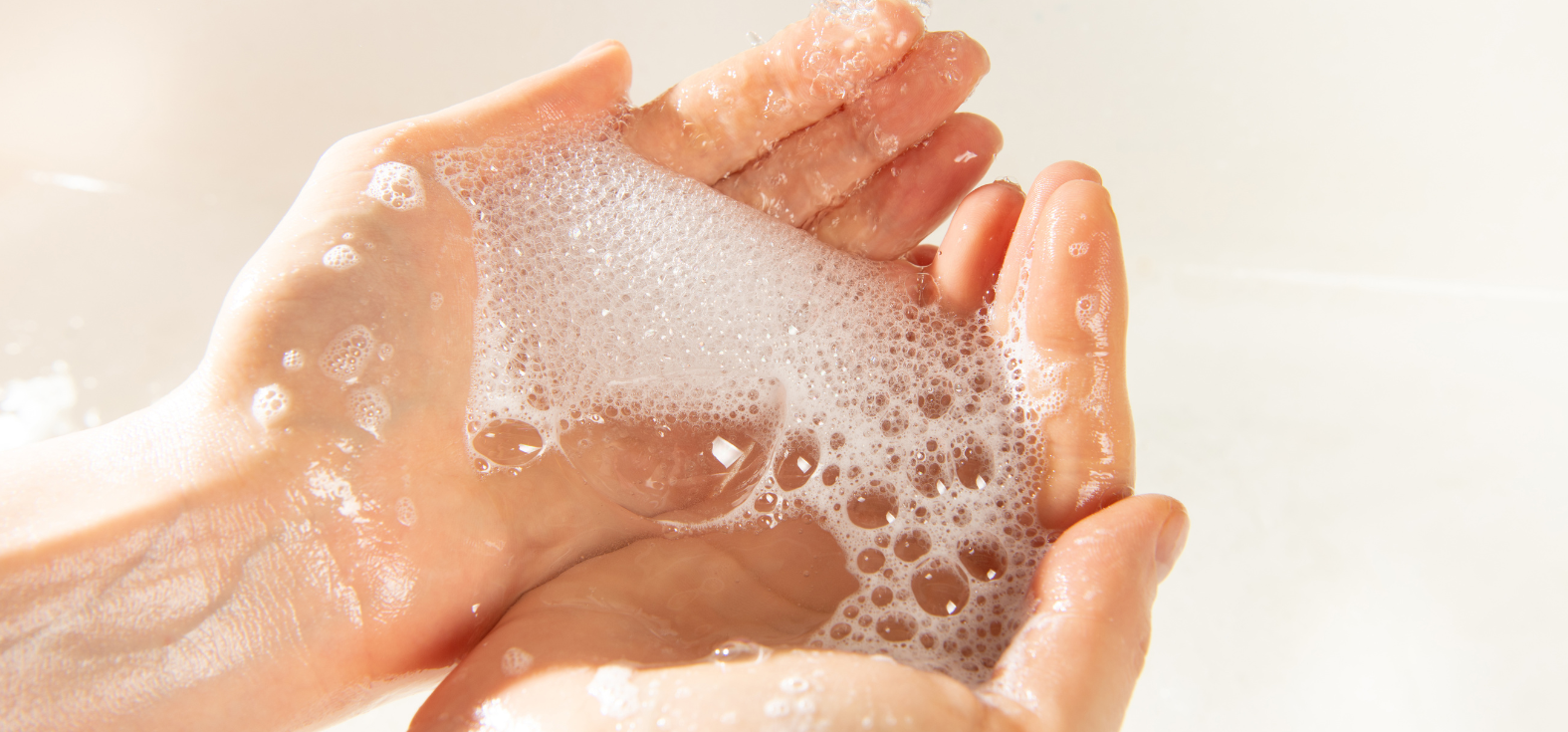 Woman holding soap suds and water in a sink as she washes her hands.